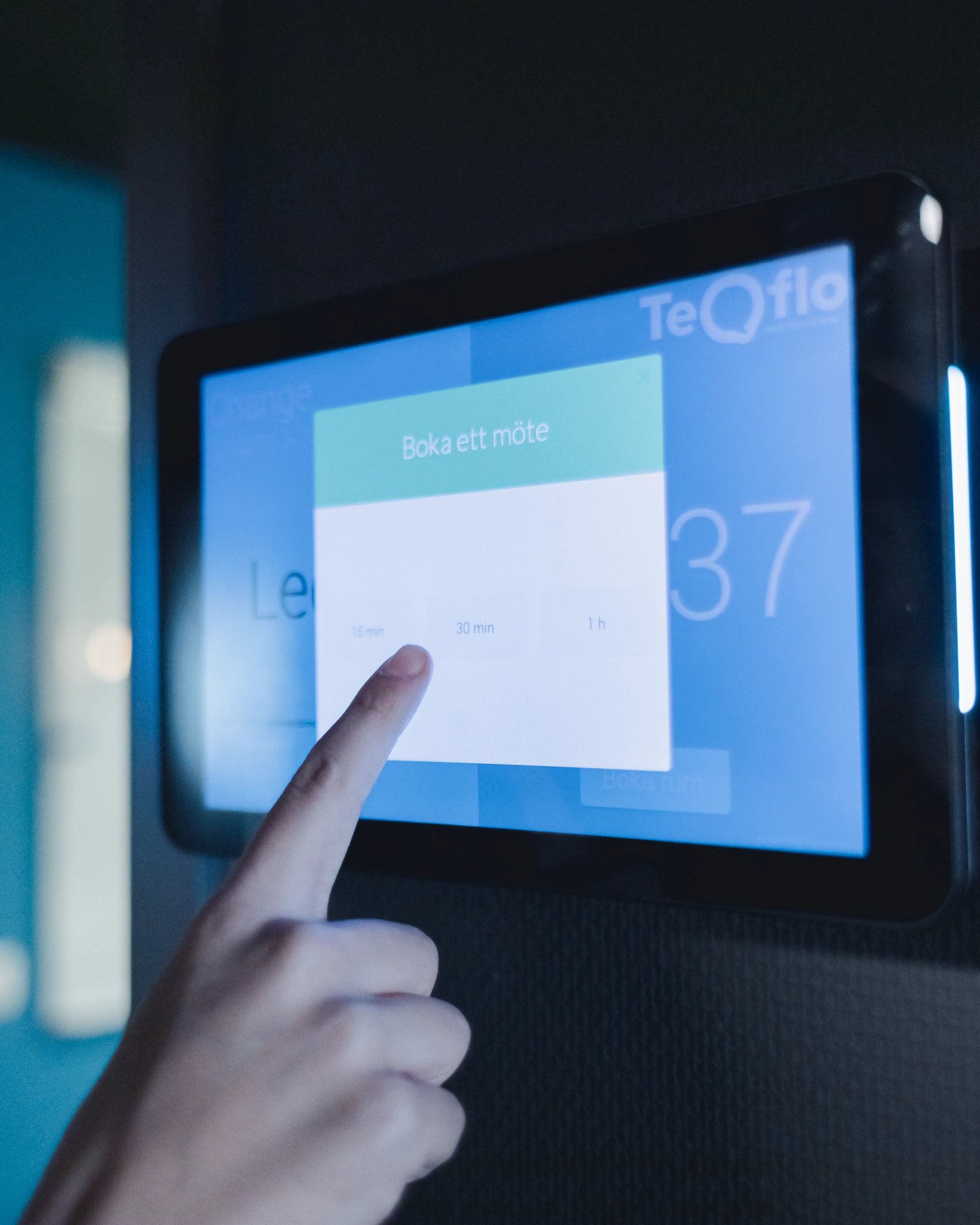 An image of a finger pressing a small screen on the wall of TeQflo's office