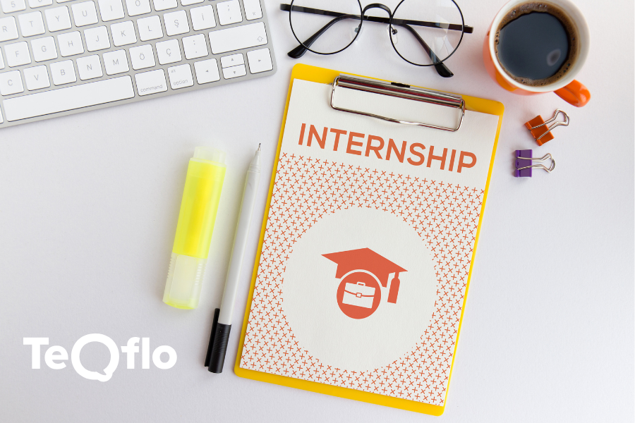 A view of a desk with a keyboard, pens, a coffee cup, and an A4 paper with the word 'INTERNSHIP' written on it.
